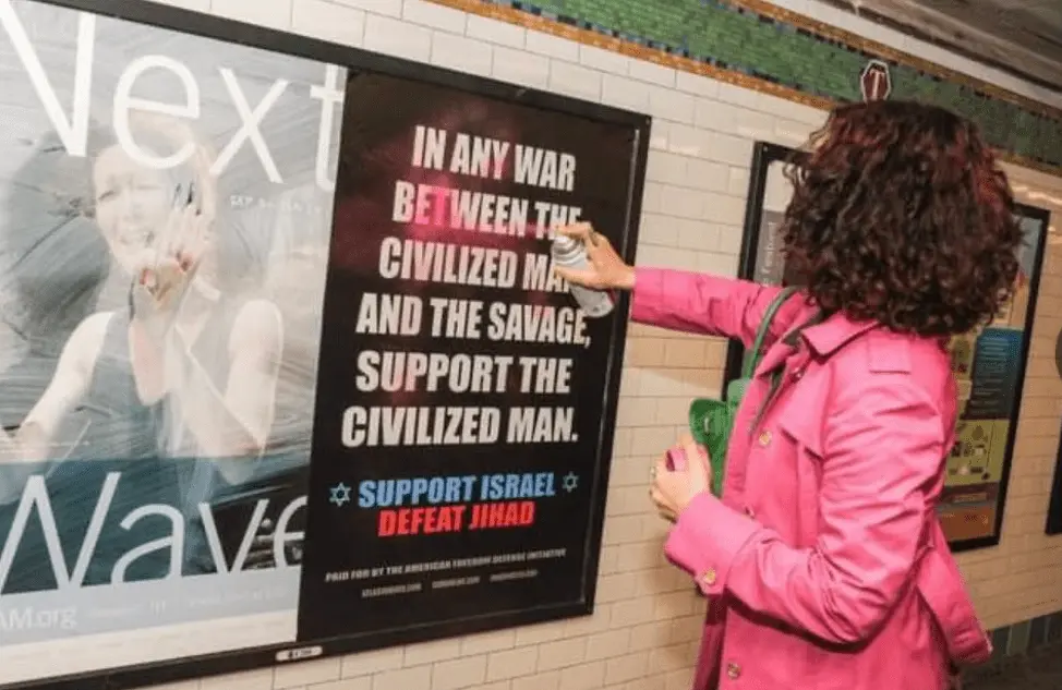 A woman in pink shirt vandalises a racist poster planted by Zionists.